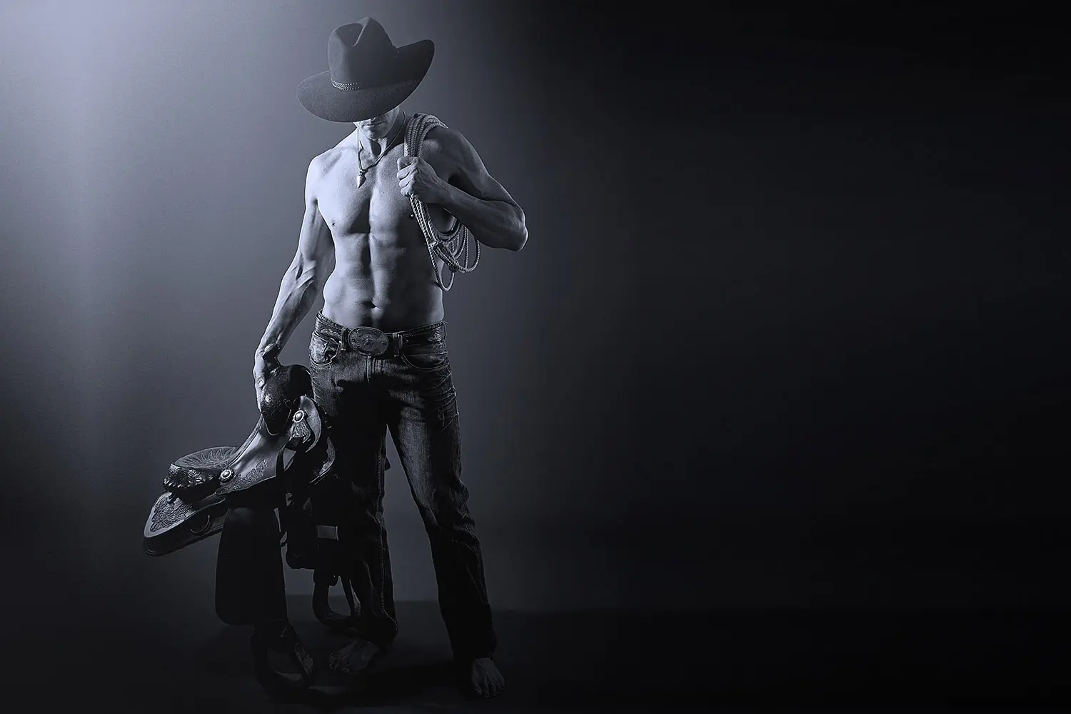 Muscular cowboy without top holding saddle and whip